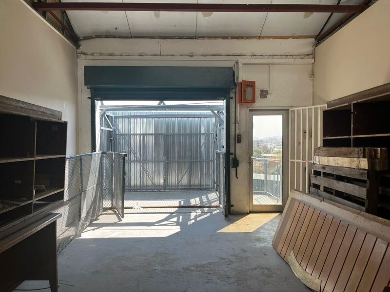 Industrial-style garage space featuring a roller shutter door, concrete flooring, and exposed ceiling beams, suitable for storage or workshop use.