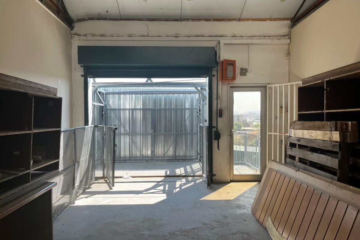 Industrial-style garage space featuring a roller shutter door, concrete flooring, and exposed ceiling beams, suitable for storage or workshop use.