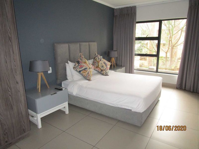 A well-maintained bedroom featuring tiled flooring, a large window with curtains, and a built-in wardrobe.