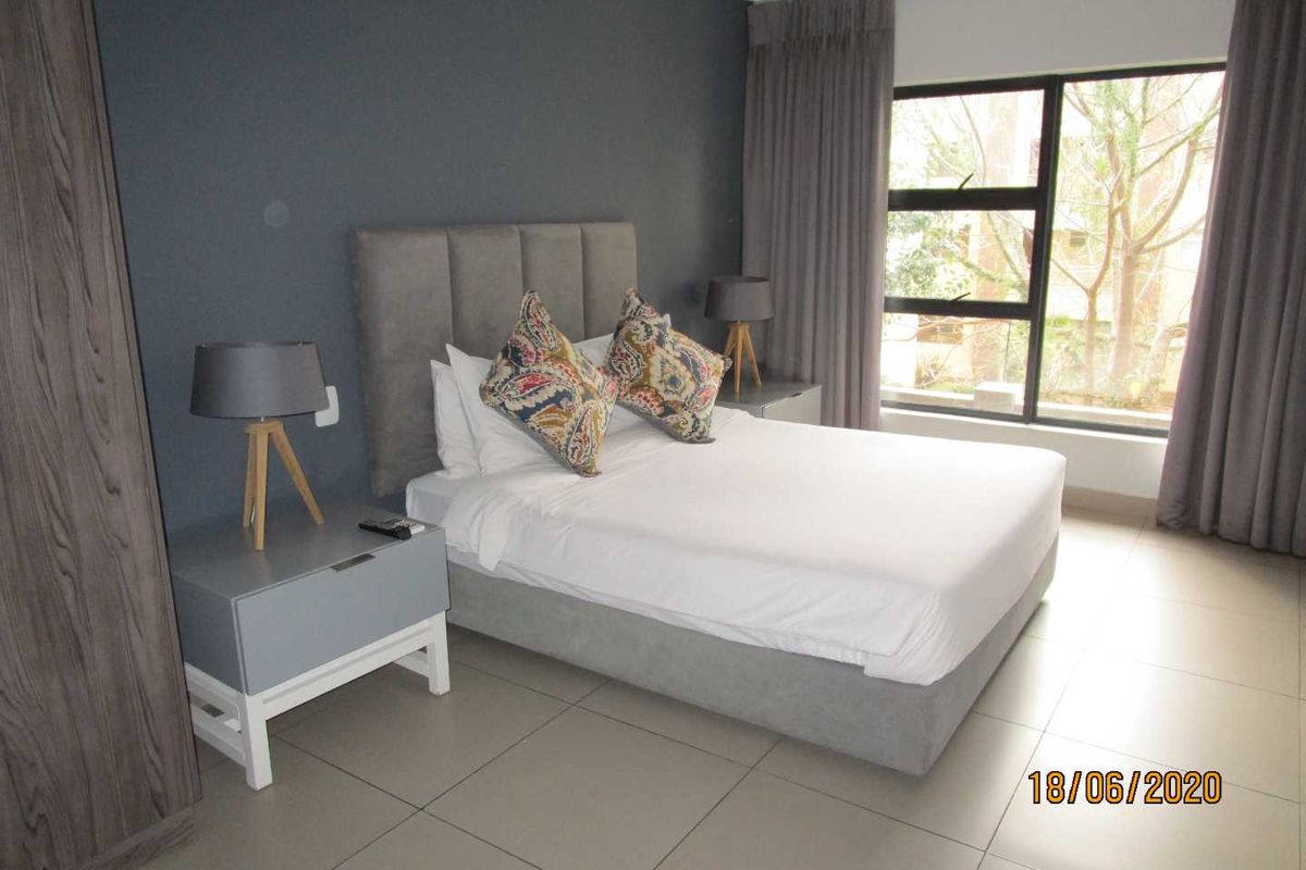 A well-maintained bedroom featuring tiled flooring, a large window with curtains, and a built-in wardrobe.