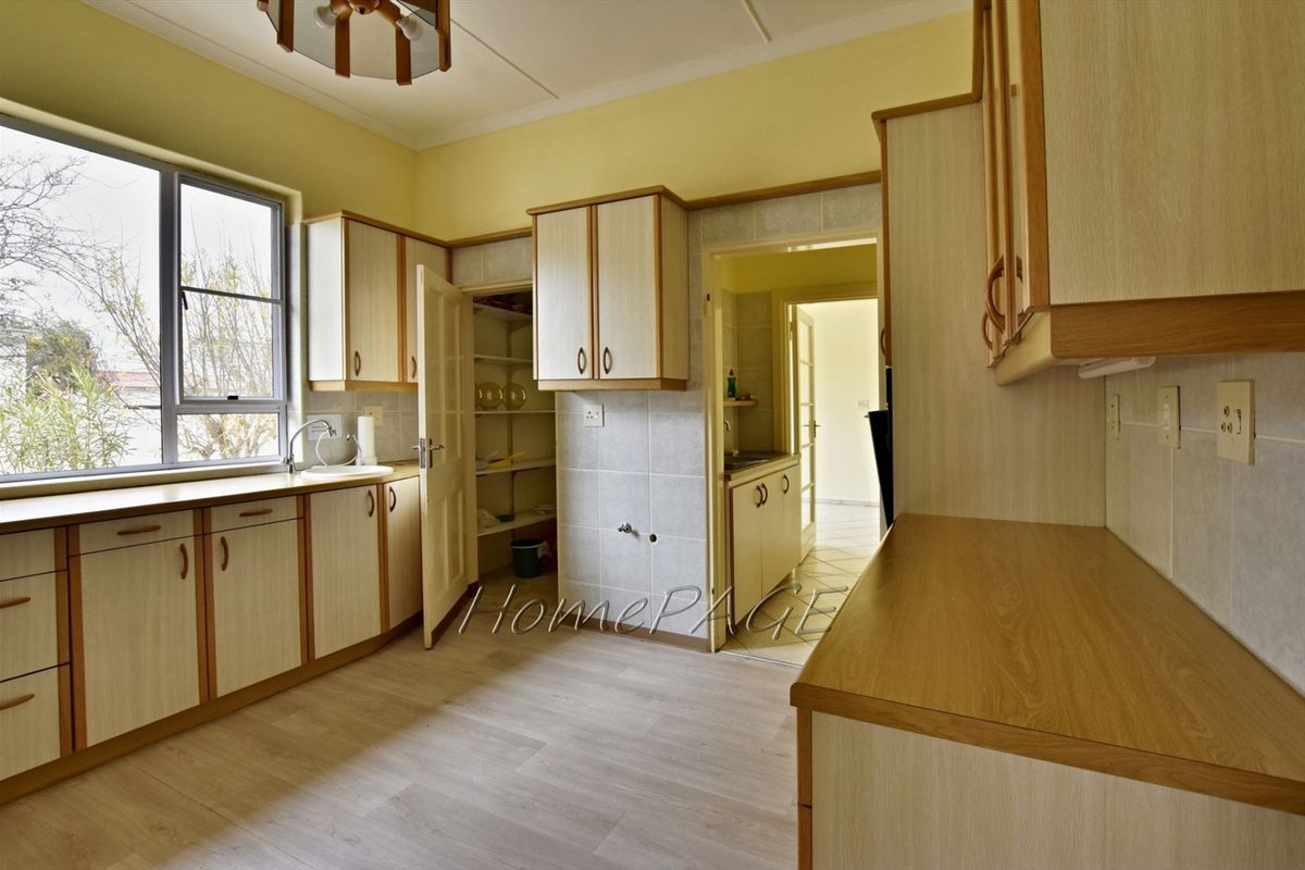 A functional kitchen featuring light wood-look cabinetry, laminate countertops, a built-in pantry, and a view through to an adjacent utility area.