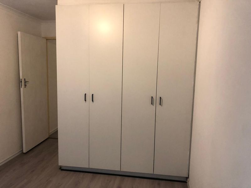 A bedroom featuring light-toned laminate flooring and a large, white built-in wardrobe with modern handles.