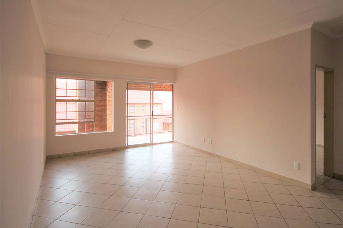 A bright, empty living room featuring neutral tiled flooring, a ceiling light fixture, and a sliding glass door leading to a balcony.