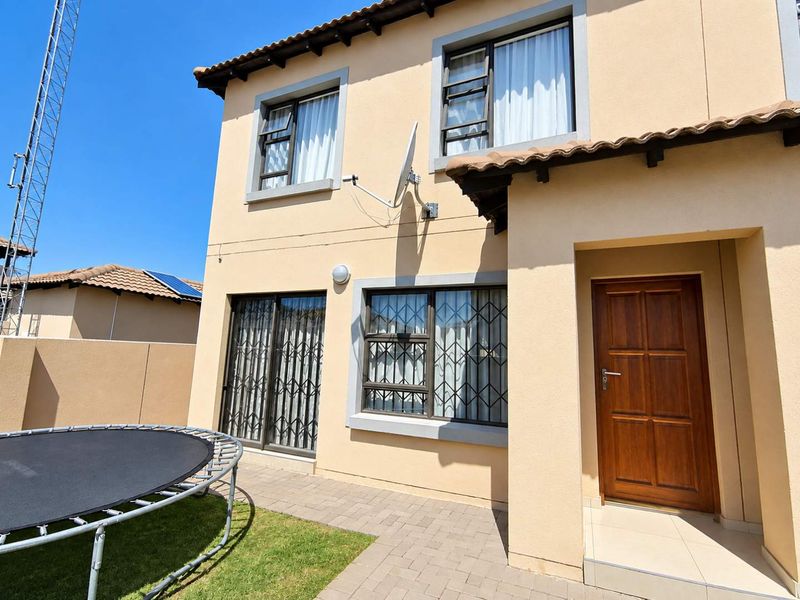 Rear view of a two-story townhouse featuring a paved patio, security-fitted windows, and a wooden entrance door.