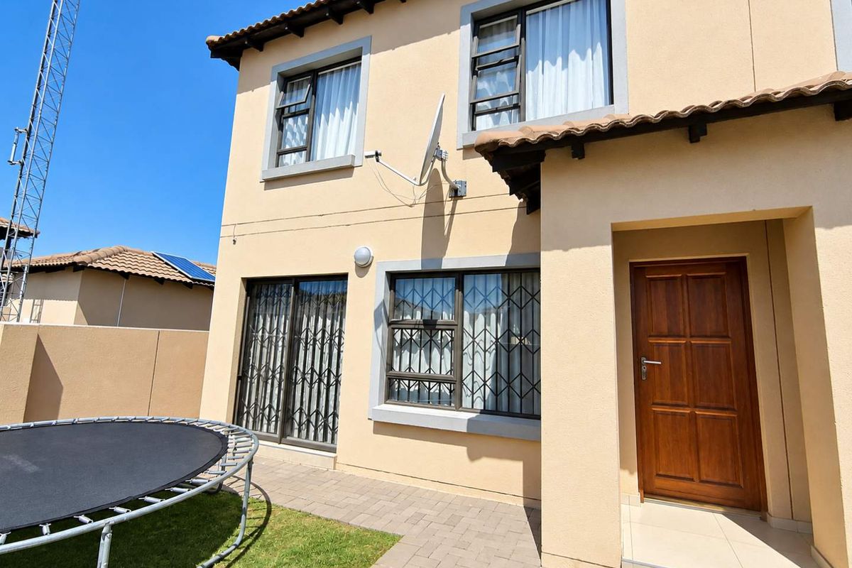 Rear view of a two-story townhouse featuring a paved patio, security-fitted windows, and a wooden entrance door.
