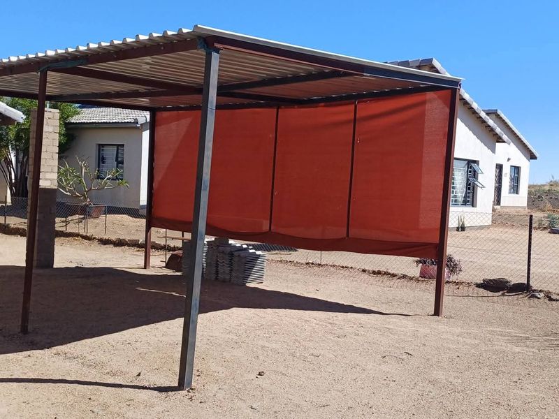 A simple outdoor covered patio area featuring a corrugated metal roof supported by steel posts and a privacy shade cloth screen.
