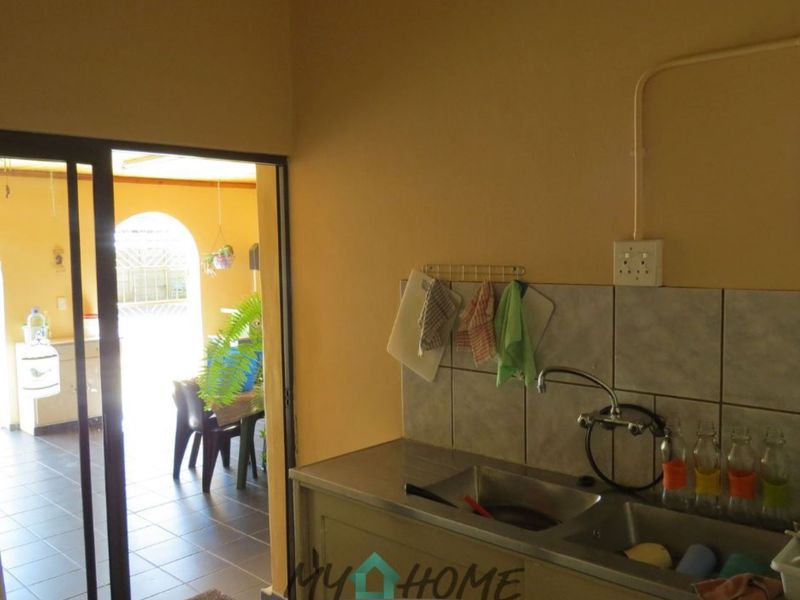 A functional scullery area featuring a double-basin stainless steel sink, tiled splashback, and direct access to an adjacent outdoor patio space.