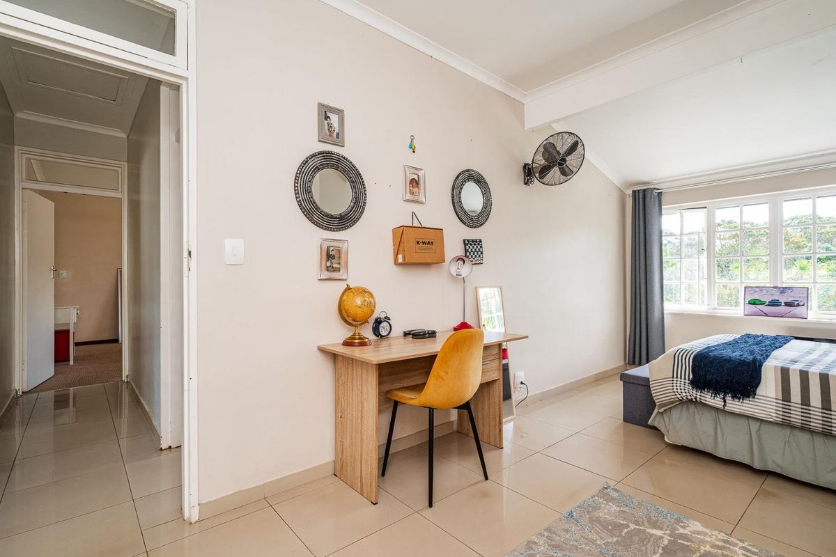 A well-lit bedroom featuring tiled flooring, neutral wall finishes, and a wall-mounted fan, offering a comfortable and functional living space.