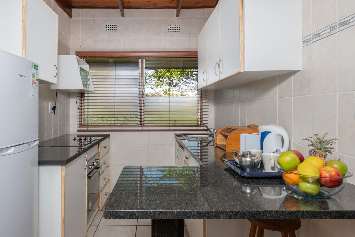 Compact kitchen featuring dark granite countertops, white cabinetry, built-in oven and hob, and tiled walls with a window overlooking the exterior.
