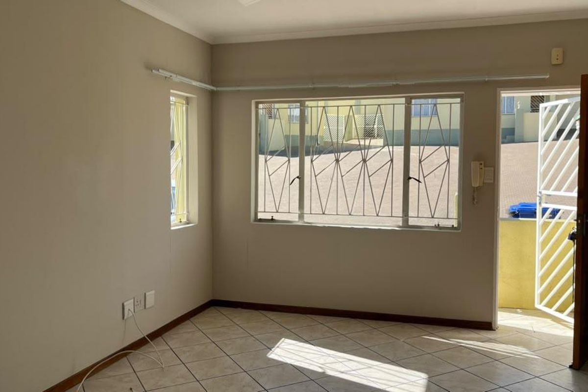 An empty living area featuring tiled flooring, security bars on windows, and a security gate leading to the exterior.