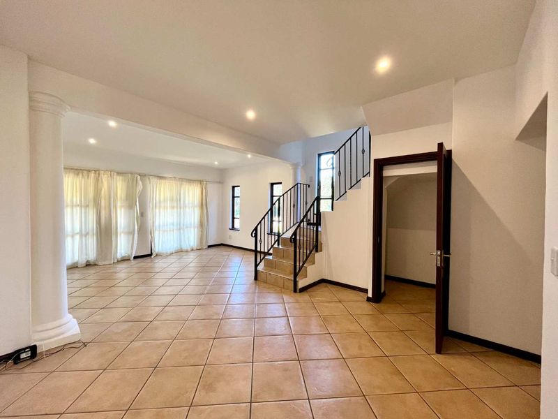 Spacious open-plan living area featuring neutral tiled flooring, a decorative column, and a staircase with wrought iron balustrades leading to the upper level.