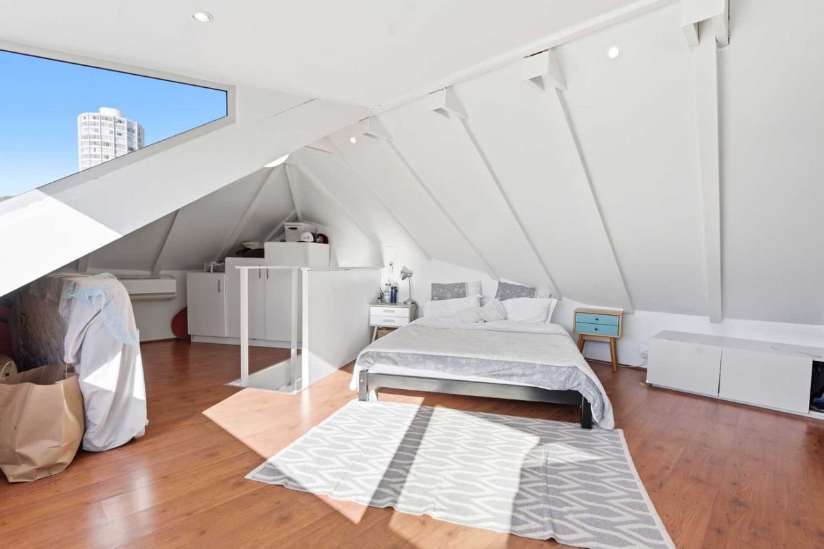 A bright attic-style bedroom featuring sloped ceilings, recessed lighting, laminate flooring, and a unique triangular window with built-in storage cabinetry.