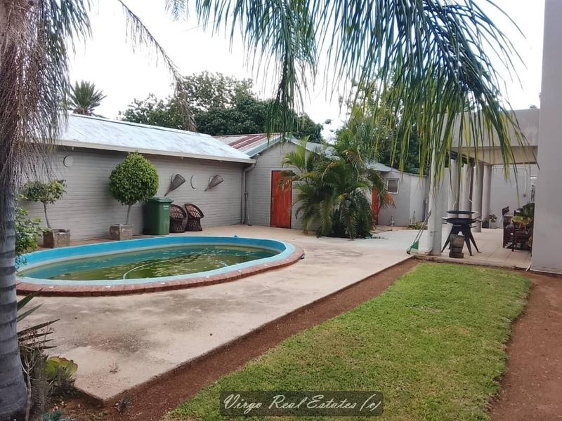 Outdoor pool area featuring a swimming pool, concrete patio, and covered outdoor space, set within a garden environment.
