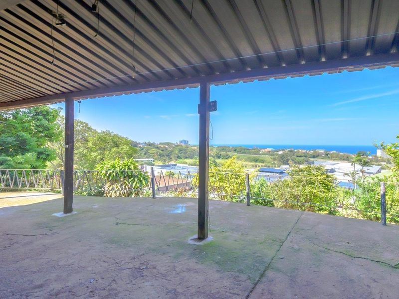 Covered outdoor patio featuring a corrugated metal roof, timber support posts, and expansive elevated views of the surrounding landscape and coastline.