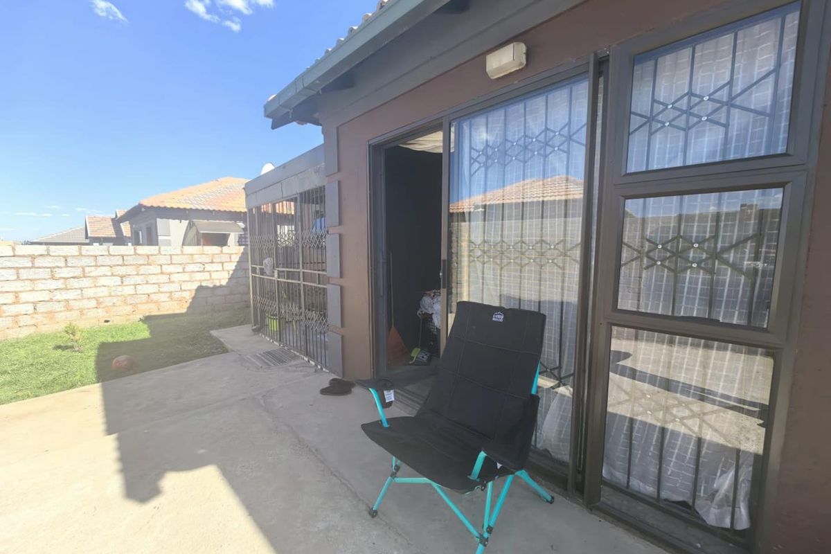 A rear exterior view of the property featuring a concrete patio area, sliding glass doors with security gates, and a brick boundary wall.