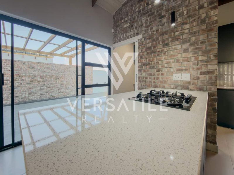 Modern kitchen featuring a stone island with integrated gas hob, exposed brick wall, and large sliding doors opening to an outdoor patio area.