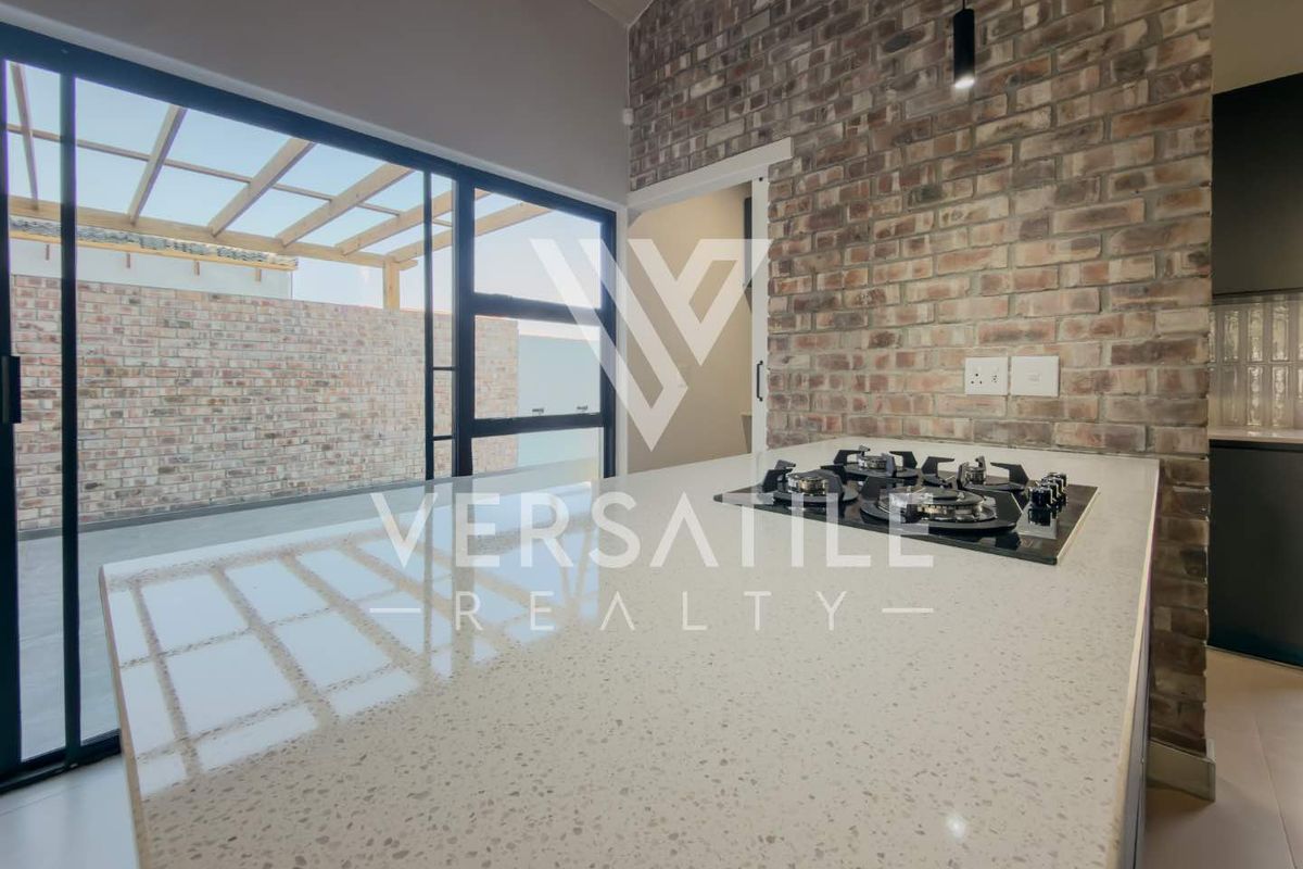 Modern kitchen featuring a stone island with integrated gas hob, exposed brick wall, and large sliding doors opening to an outdoor patio area.