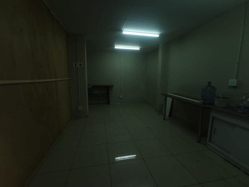 A dimly lit, vacant utility or storage space featuring tiled flooring and basic electrical infrastructure, suitable for various commercial storage or workspace applications.