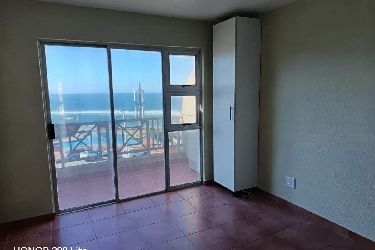 A bright, empty bedroom featuring tiled flooring, a built-in cupboard, and sliding glass doors that open onto a balcony with ocean views.