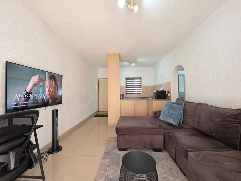 Open-plan living area featuring tiled flooring, textured walls, and a compact kitchen space with built-in cabinetry and sink.