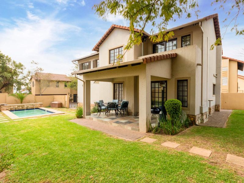Rear view of the property featuring a covered patio, a well-maintained garden, and a private swimming pool with stone water feature.