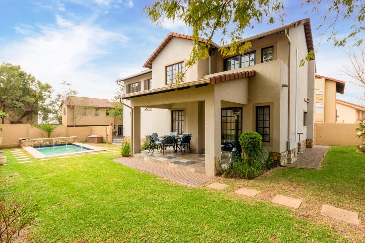 Rear view of the property featuring a covered patio, a well-maintained garden, and a private swimming pool with stone water feature.