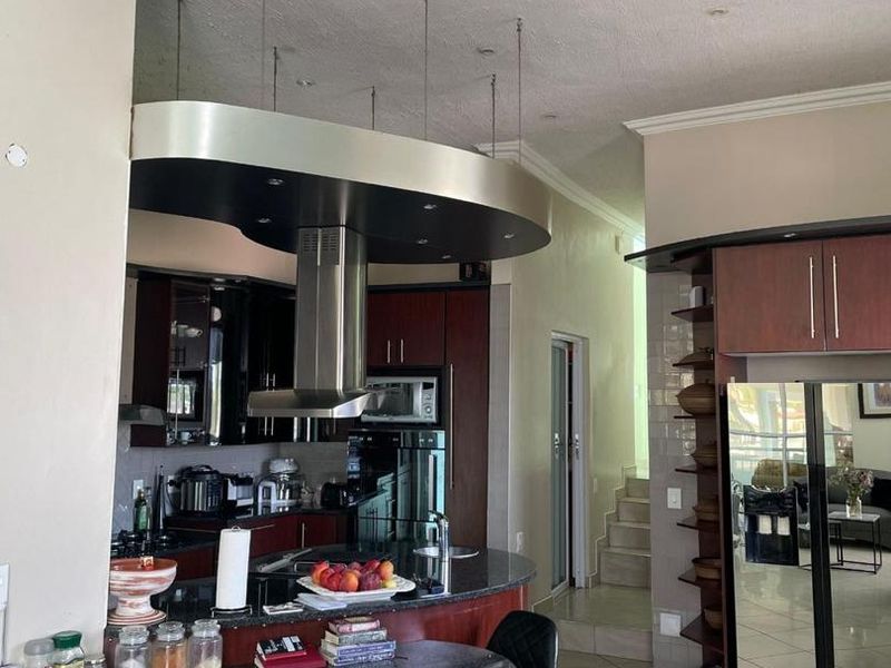 A kitchen featuring dark wood cabinetry, granite countertops, a central island with an overhead extractor fan, and tiled flooring.