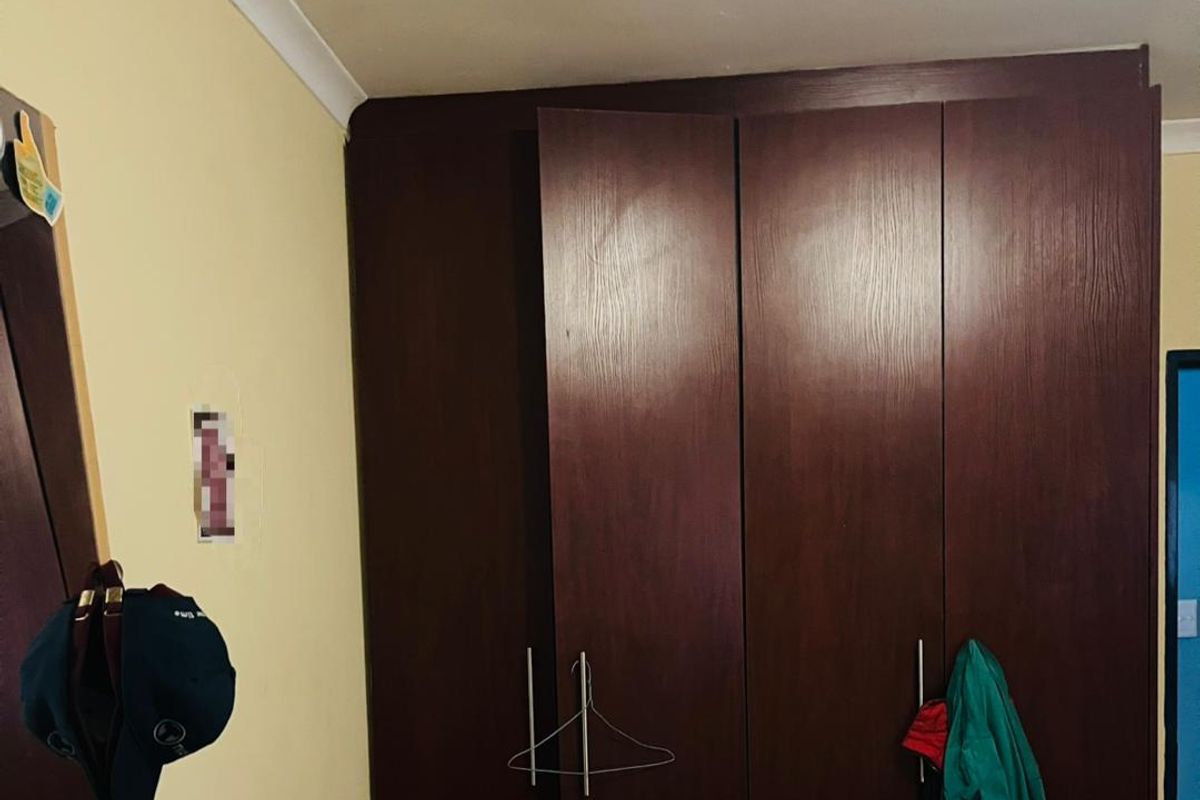 A bedroom featuring a large, dark wood-finish built-in wardrobe providing ample storage space.