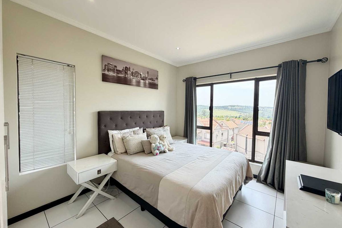 A well-maintained bedroom featuring tiled flooring, recessed lighting, and a large window with blinds and curtains, offering pleasant views of the surrounding neighborhood.