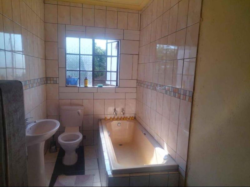A functional bathroom featuring a pedestal basin, toilet, and built-in bathtub with tiled walls and flooring.