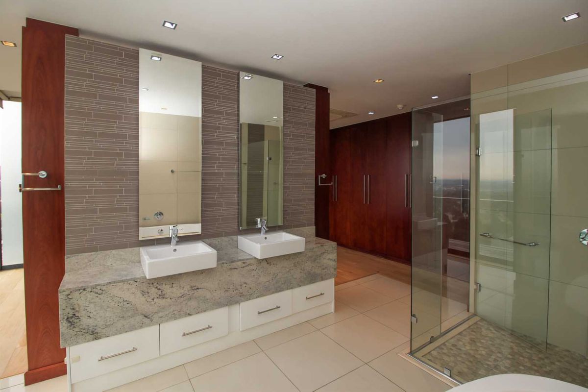 Modern penthouse bathroom featuring a double vanity with granite countertop, vessel sinks, glass-enclosed shower, and extensive built-in cabinetry.