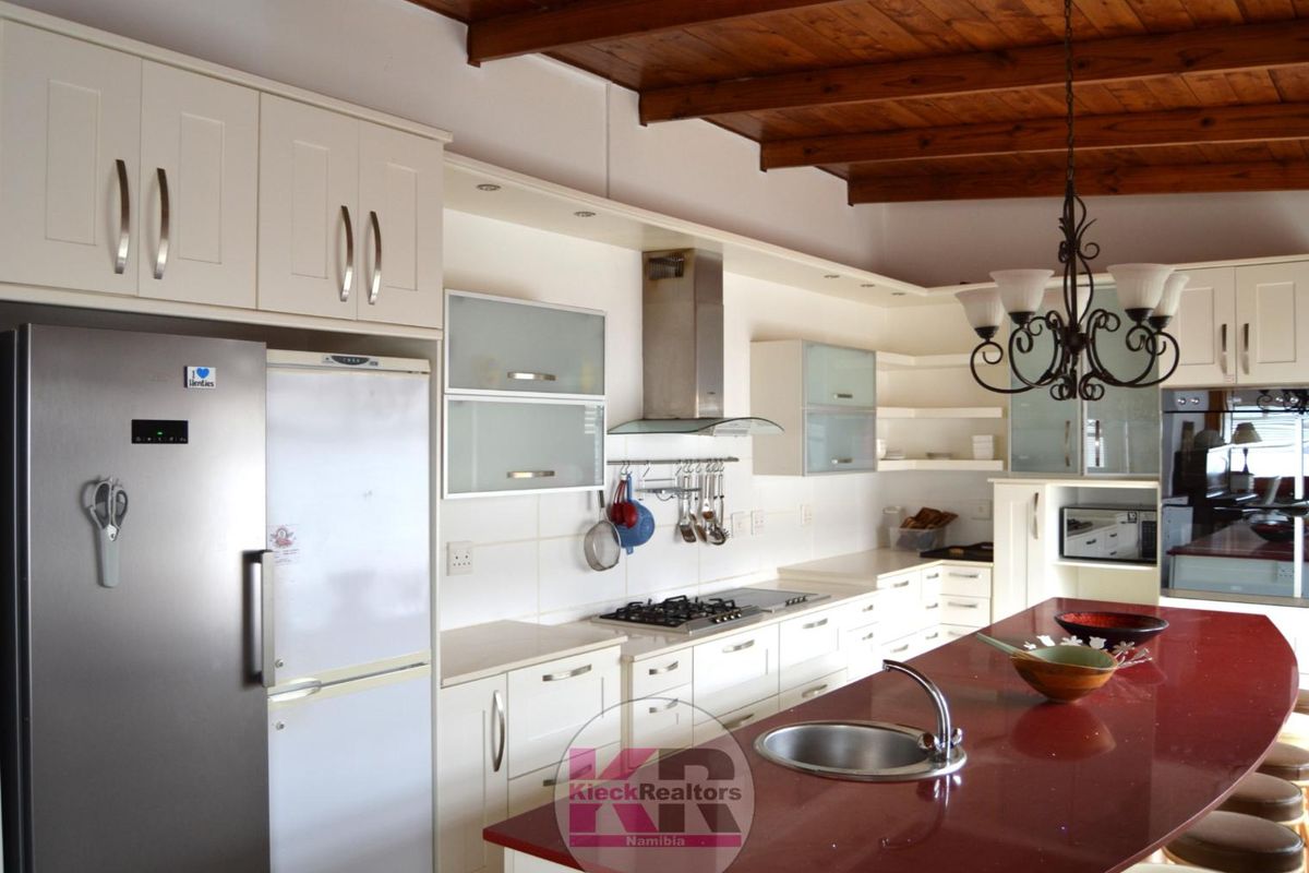 Spacious kitchen featuring white cabinetry, a large island with a red countertop, gas hob, extractor fan, and exposed timber ceiling beams.
