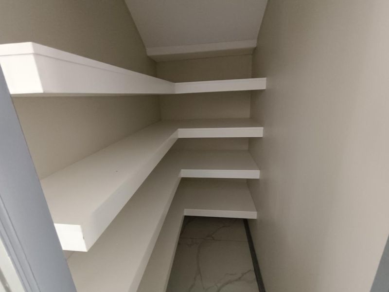 A compact, empty storage pantry or scullery area featuring clean white built-in shelving and modern tiled flooring.