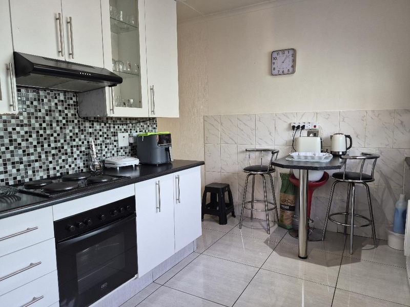 A functional kitchen featuring white cabinetry, a dark countertop, a built-in oven with hob, and a tiled backsplash with a small breakfast nook area.