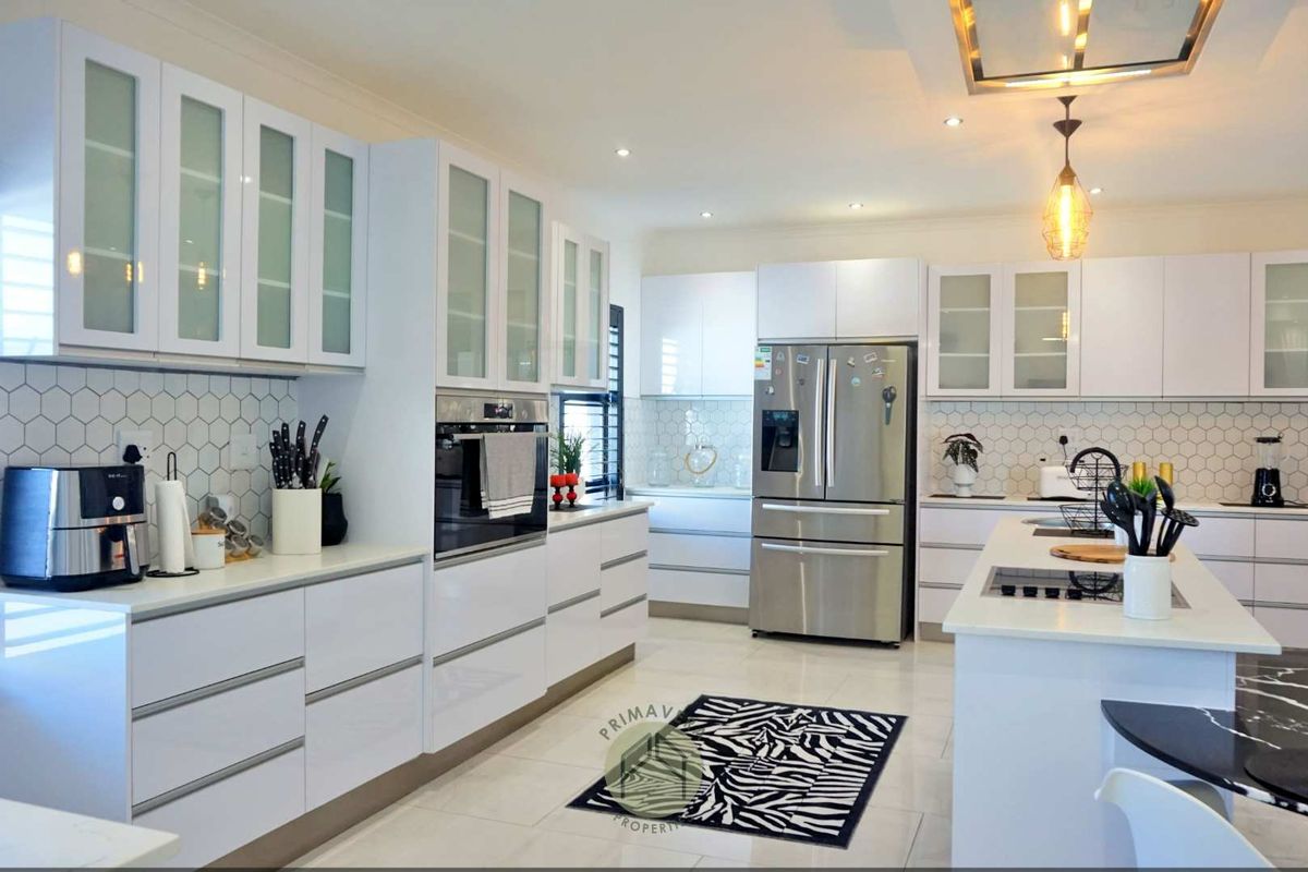 Modern kitchen featuring white cabinetry, stone countertops, a central island with a built-in hob, and integrated stainless steel appliances.