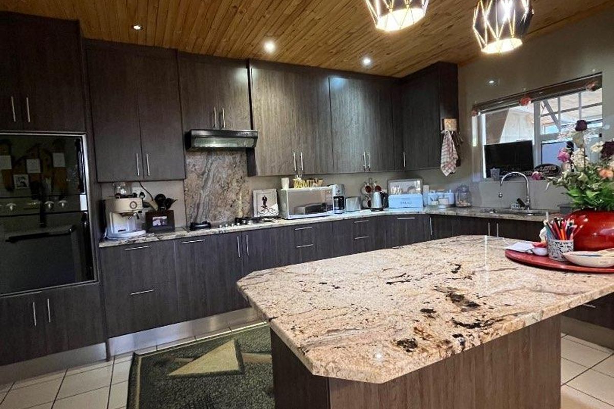 Modern kitchen featuring dark cabinetry, granite countertops, a central island, and a distinctive timber-clad ceiling with contemporary pendant lighting.