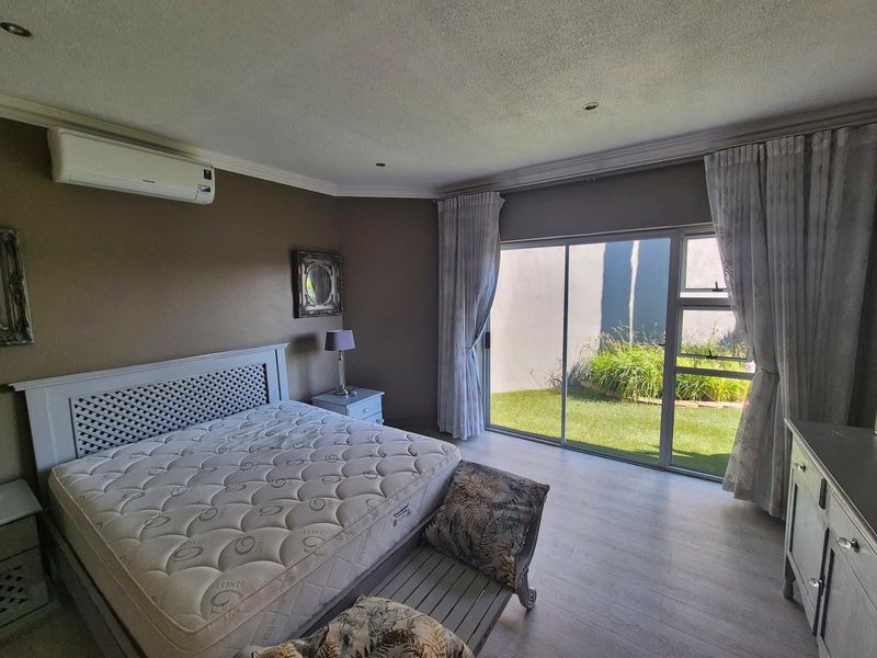 Spacious bedroom featuring laminate flooring, a wall-mounted air conditioning unit, and large sliding glass doors providing direct access to the garden area.