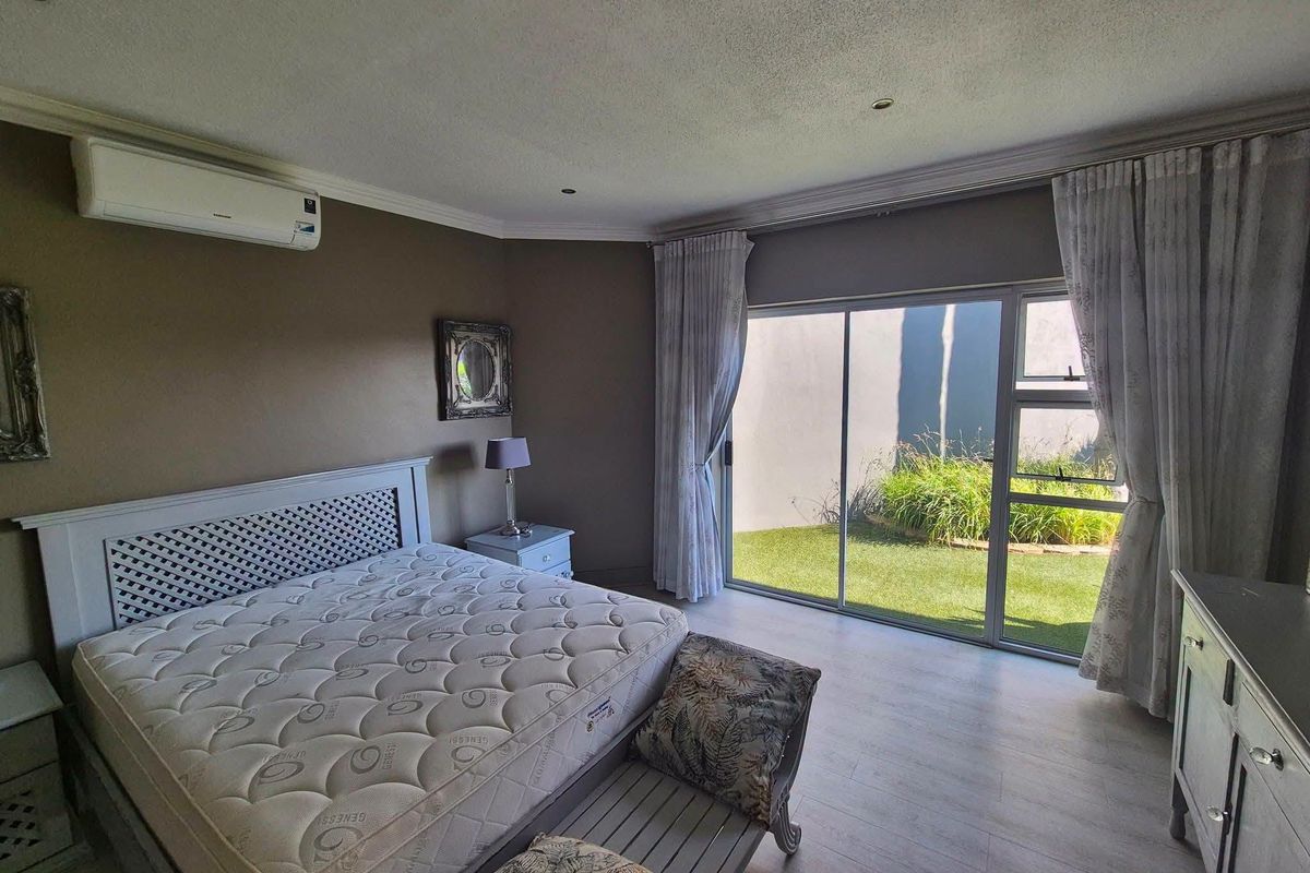 Spacious bedroom featuring laminate flooring, a wall-mounted air conditioning unit, and large sliding glass doors providing direct access to the garden area.