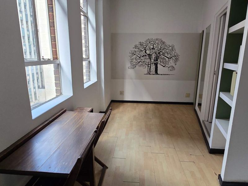 A bright, empty living area featuring laminate flooring, built-in shelving, and large windows that provide ample natural light.