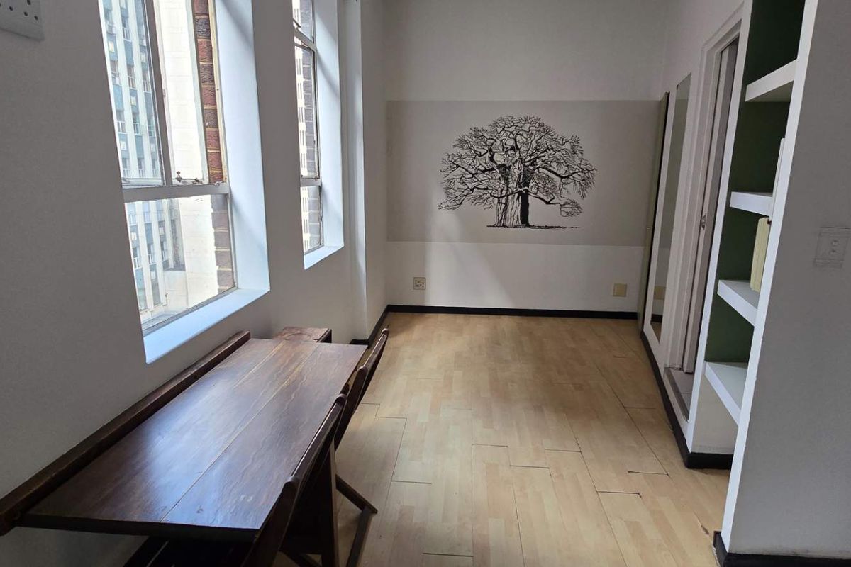 A bright, empty living area featuring laminate flooring, built-in shelving, and large windows that provide ample natural light.