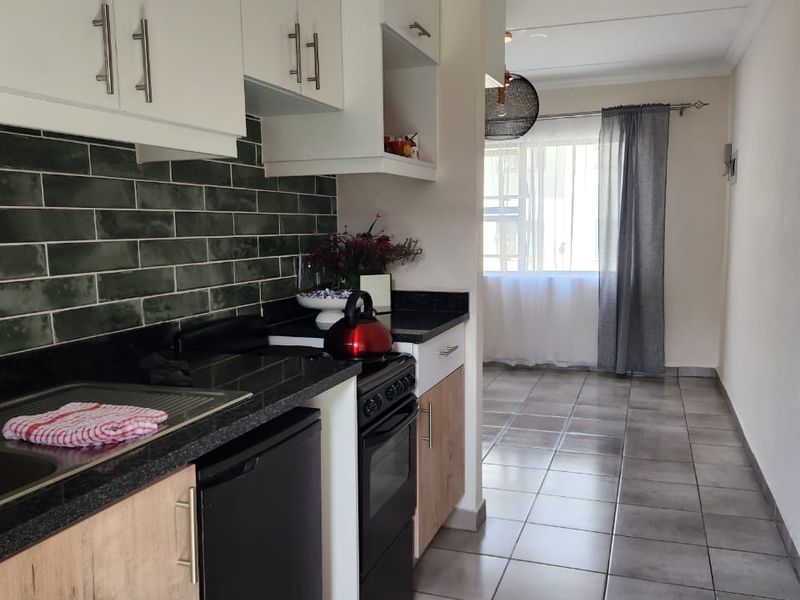 Modern kitchen featuring white and wood-tone cabinetry, dark granite countertops, green subway tile backsplash, and durable ceramic floor tiles.