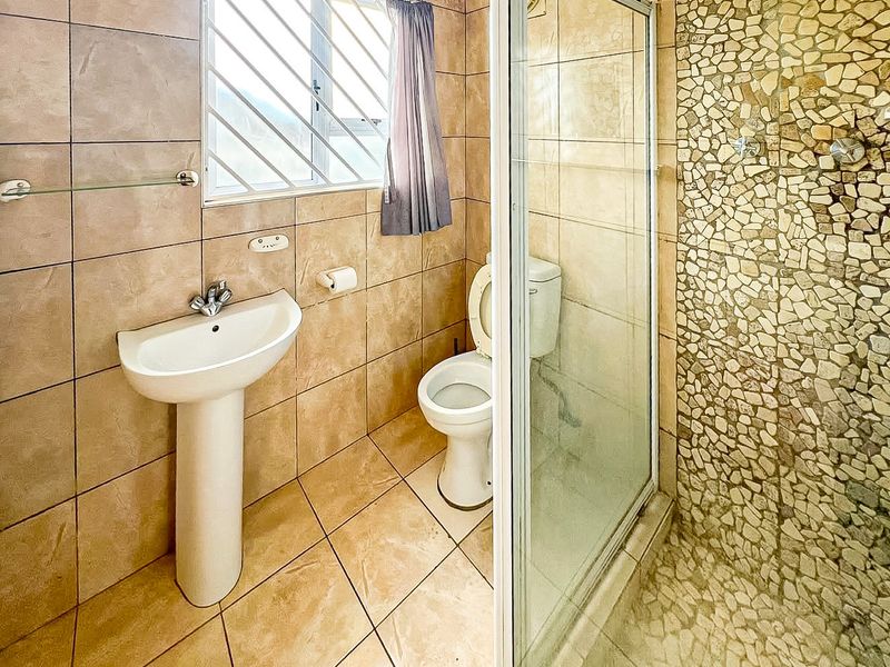 A functional bathroom featuring a pedestal basin, toilet, and a shower enclosure with a decorative stone mosaic feature wall and tiled finishes.