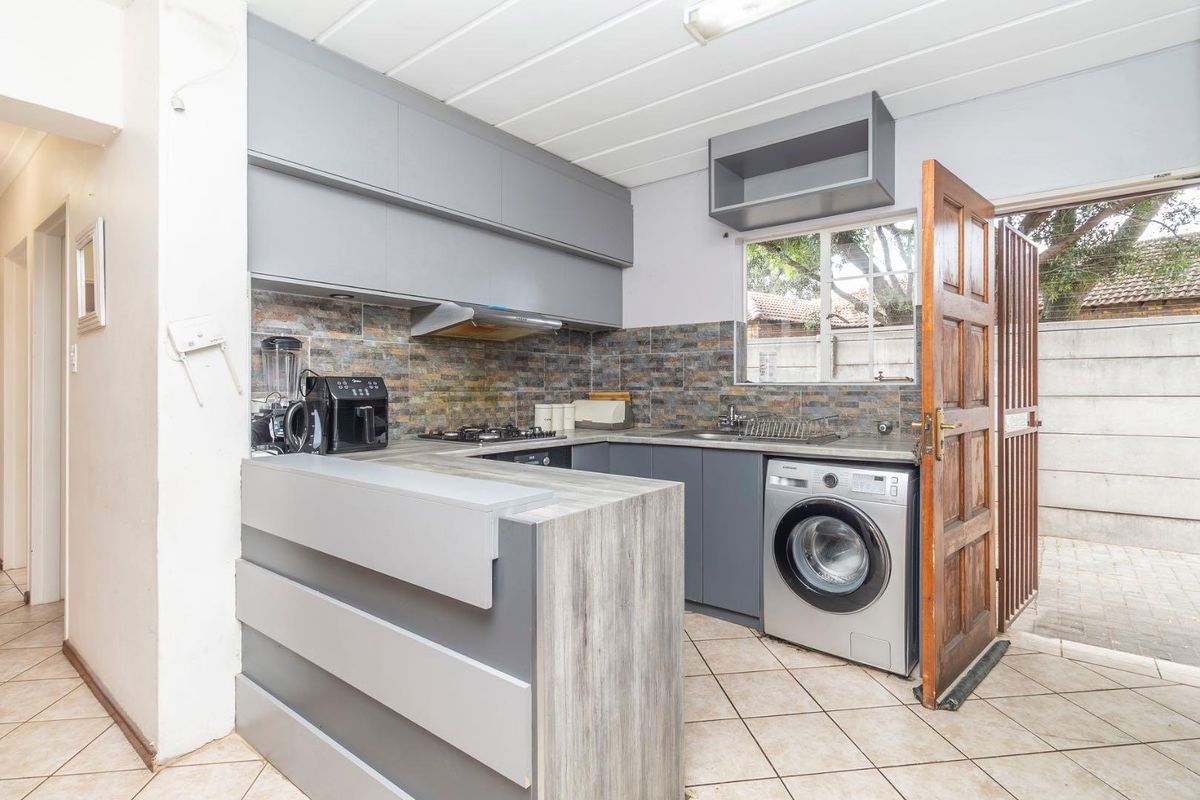 Compact kitchen featuring grey cabinetry, stone-look tiled backsplash, built-in hob, extractor fan, and integrated laundry plumbing with direct access to the rear exterior.