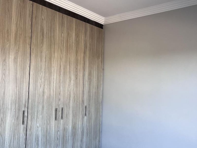 A clean, empty bedroom featuring modern wood-finish built-in cupboards, tiled flooring, and decorative ceiling cornicing.