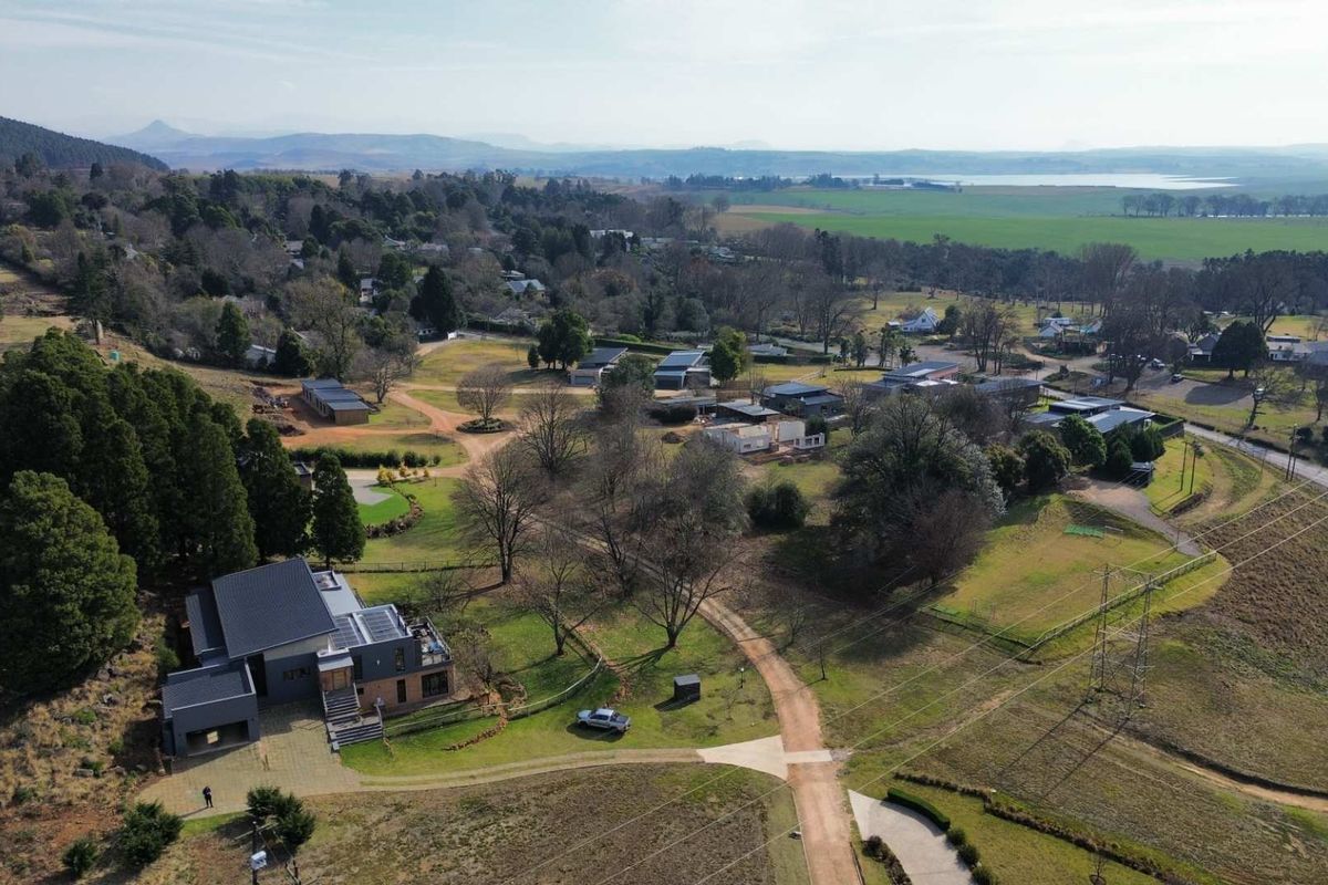 Aerial view of a residential property featuring a modern home with solar panels, surrounded by expansive green landscape and rural surroundings.