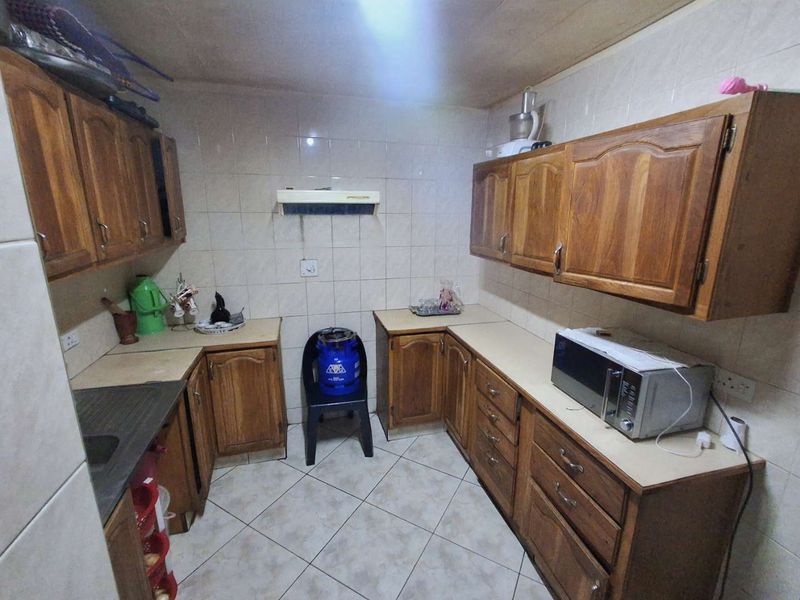 A functional kitchen featuring traditional wooden cabinetry, tiled backsplash, and tiled flooring, offering a dated aesthetic with potential for modern renovation.