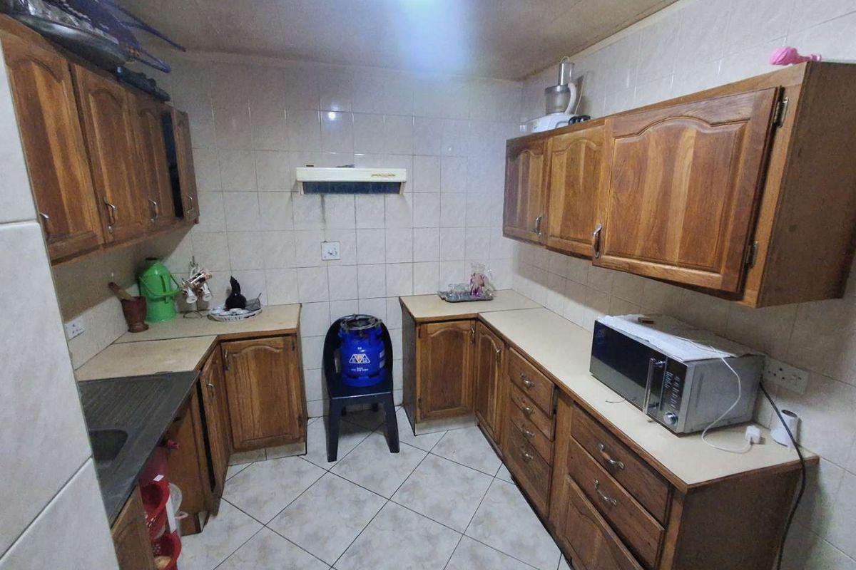 A functional kitchen featuring traditional wooden cabinetry, tiled backsplash, and tiled flooring, offering a dated aesthetic with potential for modern renovation.