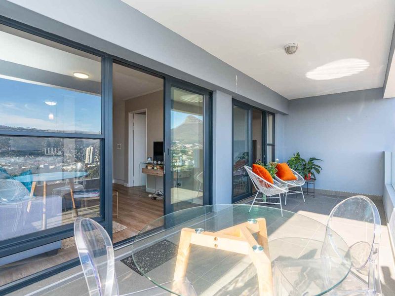 A spacious covered balcony featuring a glass balustrade, tiled flooring, and large sliding doors providing seamless access to the interior living area.