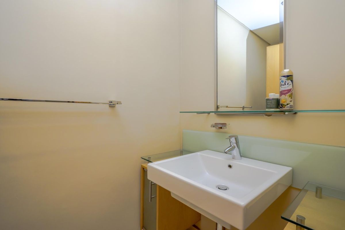 A clean and functional bathroom featuring a modern wall-mounted basin, chrome mixer tap, glass splashback, and a large wall mirror.