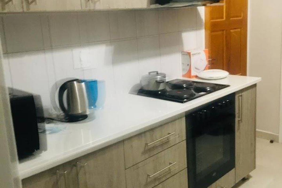 A functional kitchen featuring light wood-grain cabinetry, a built-in oven, electric hob, extractor fan, and white tiled splashbacks.
